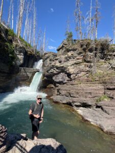 Young man standing on a rock in front of a waterfall at Glacier National Park. 